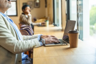 Senior professional working remotely at a busy coworking table, focused on laptop and video call