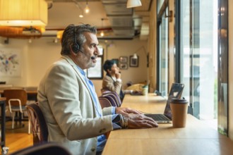 Mature man wearing a headset and working on a laptop in a modern coworking space, focused on a