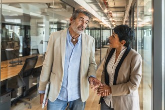 Mature business colleagues walking down a modern office corridor, having an engaging discussion and