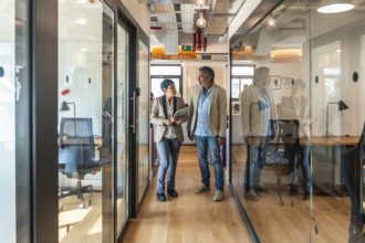 Two diverse business colleagues, a man and a woman, walking along a glass walled corridor in a