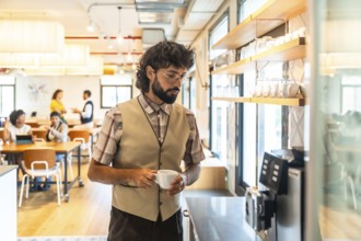 Young adult man with a beard and glasses holding a coffee cup. Preparing a drink at a coffee