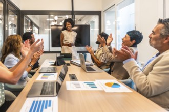 Diverse business professionals applaud a smiling female leader at a conference table after her