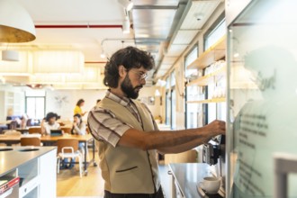 Bearded man preparing coffee at a modern coworking space, taking a relaxed break from work while