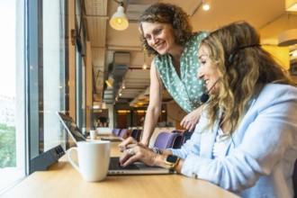Two smiling women are collaborating and supporting each other while wearing headsets, working on
