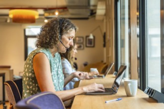 Women concentrating on their work using laptops and headsets in a modern coworking office,