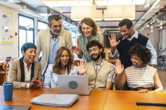 Diverse business colleagues at office desk having an online video conference, waving hands and
