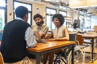 Diverse colleagues with varying abilities collaborating on a laptop in a modern coworking office,
