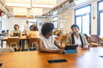 Diverse colleagues engaged in conversation and working on digital devices while collaborating at a