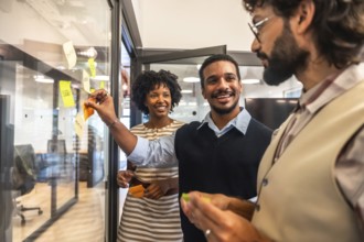 Diverse business colleagues collaborating on a project, smiling and applying colorful sticky notes