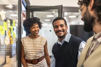 Coworkers smiling and engaging in discussion, brainstorming ideas on a glass board with sticky