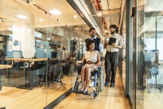 Diverse business colleagues pushing a young black woman in a wheelchair through a modern,