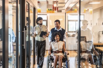 Diverse office colleagues walking together, two men assisting a smiling woman in a wheelchair,