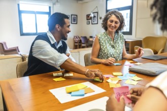 Diverse coworkers sitting around a wooden table, smiling and collaborating on new project ideas