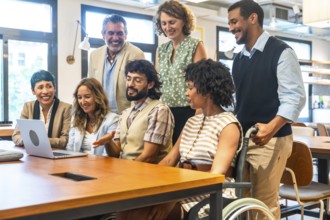 Diverse corporate team smiling and collaborating around a laptop in an inclusive coworking office,