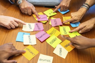 Business colleagues gathered around a wooden table point at colorful sticky notes labeled planning,