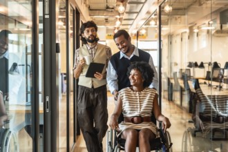 Diverse business colleagues pushing a smiling woman in a wheelchair through a modern office