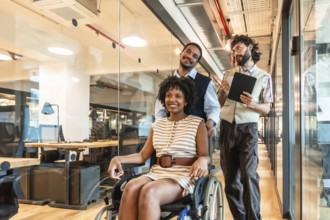 Diverse business colleagues pushing a smiling woman in a wheelchair through a contemporary office
