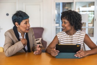Two diverse women colleagues collaborating and talking about business while sitting at a table in