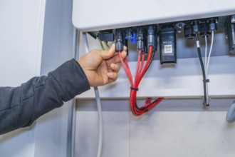 Hand connects red cables to a Solax system in a control box