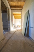 A shell with sunlight in the corridor. Cables, unfinished walls and a wooden floor define the room