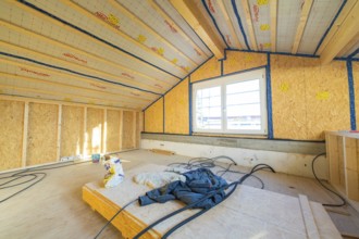 Unfinished construction of an attic with insulation on the walls. Large windows let in lots of