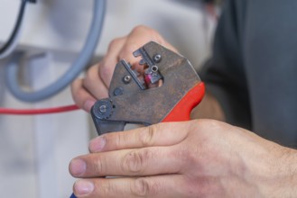 Hand holding pliers that process a cable, industrial environment
