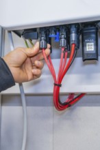 Hand connects several red cables to plugs in a control cabinet