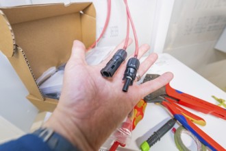 Electrician holds plugs and cables, tools and materials in the background
