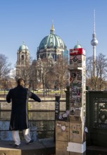 A man stands next to a demolished modern Telekom telephone column, view of Lustgarten Cathedral,