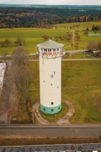 White water tower in rural autumn landscape with green fields and autumnal trees, water tower,