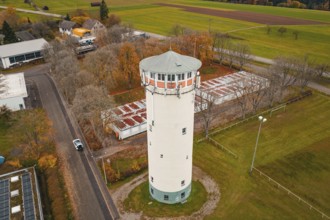 Water tower on a road with autumn trees in rural area, surrounded by small buildings, water tower,