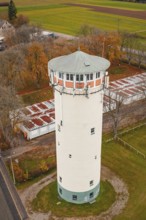 Close-up of a water tower surrounded by trees with autumn leaves, next to buildings with red roofs,