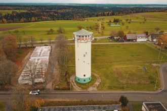 Water tower in the middle of a vast landscape with fields and small buildings in the background,