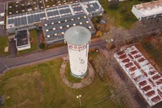 Aerial view of a water tower and surrounding buildings with rusty roofs and solar panels, water