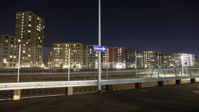 One way street on the fence, behind it a passing ICE train, illuminated apartments in a new housing