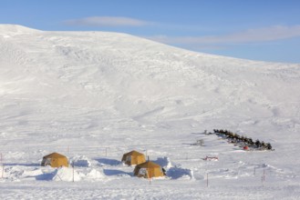 Snowmobiles, snow scooters at Arctic expedition camp with tents protected by tripwire fence against