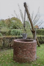 An old brick well with a bucket in an autumnal garden, Münsterland, North Rhine-Westphalia, Germany