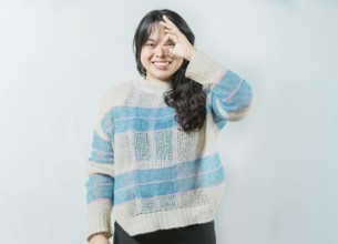 Beautiful asian woman making OK gesture looking through fingers isolated. Smiling asian girl making
