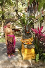 Woman holding offerings in front of a Ganesha statue, Bali, Indonesia