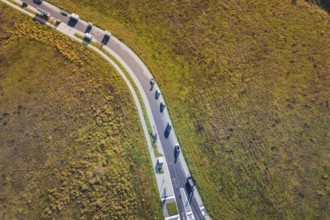 Curved road with cars through autumnal meadow landscape, new Lindenrain industrial park, Calw,