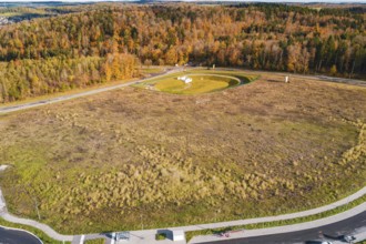 Wide meadow area surrounded by autumn-colored forest and roads, new Lindenrain industrial park,
