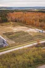 Construction site next to autumnal forest with visible earthworks and scattered trees, new