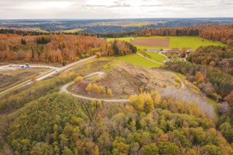 Hilly landscape with autumnal forests and open fields under cloudy sky, new Lindenrain industrial