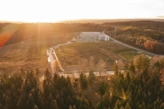 Scene at sunset with a building in the middle of a wooded landscape under soft light, new