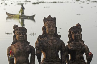 Three Hindu god statues made of clay, fishermen in a boat in the background, Vembanad Lake, Kerala,