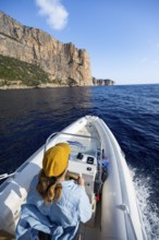 Young woman riding a motor boat along the picturesque rocky coast, cliffs and blue sea, Golfo di