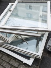 A pile of old white window frames with glass is lying on a sidewalk in Wuppertal, Germany