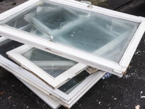A pile of old white window frames with glass is lying on a sidewalk in Wuppertal, Germany