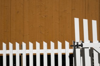 Yellow-painted wooden wall behind a white-painted fence, Maihaugen open-air museum with houses and