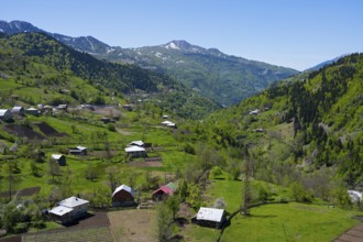 Houses and fields in a green valley in front of a mountain range, on the way to the Goderdzi Pass